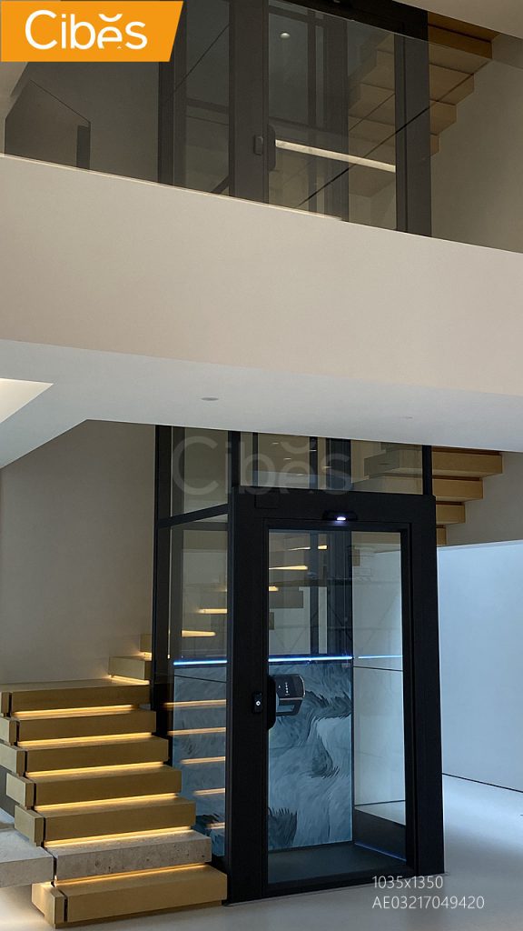 Cibes screw-driven glass home lift installed in the middle of the stair in a modern residence.
