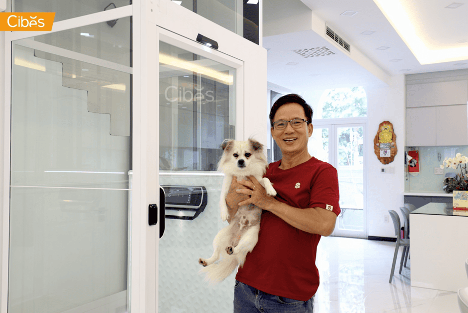 Man holding a small dog beside a home elevator in a modern house interior.